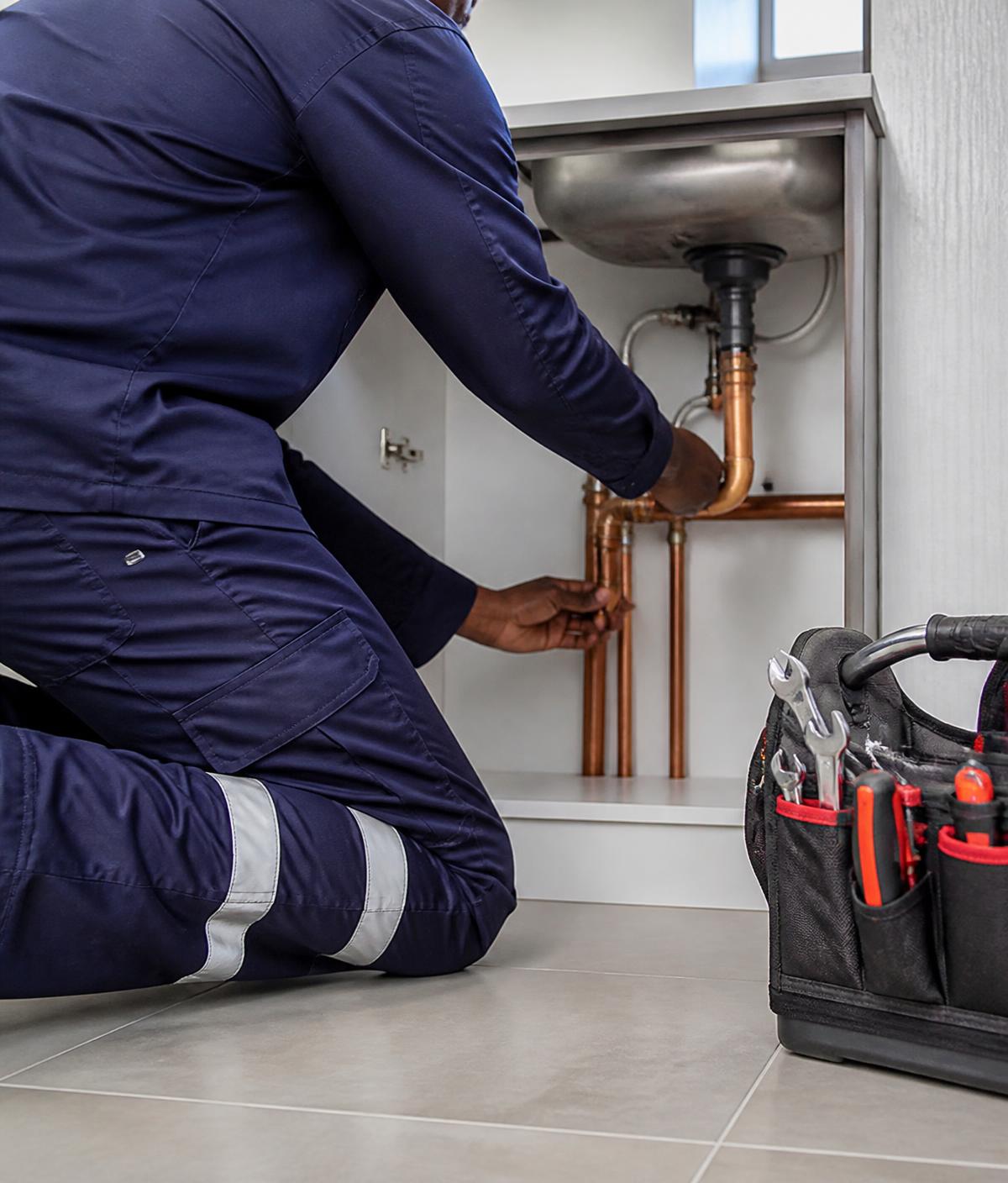 Plumber in navy overalls repairing copper water pipes under a kitchen sink in Windhoek